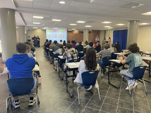 High school students sit in chairs facing a screen in the Concourse for the AMC 10 and AMC 12 Mathematics Competition.